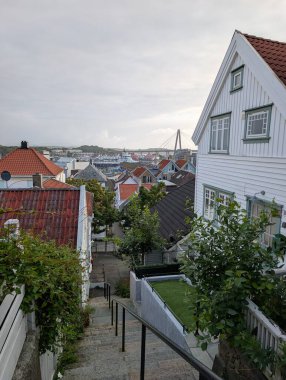Stavanger Norveç 'te. Beyaz ahşap evler ve kırmızı çatılar, kıyı kenti limanına bakan, bulutlu gökyüzünün altında köprüsü olan dik taş merdivenler..