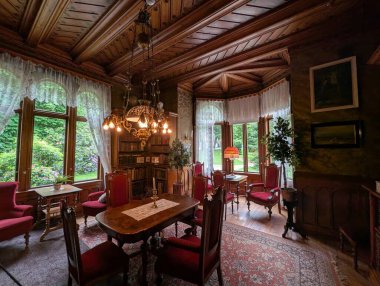 Günışığı kütüphanesinde kırmızı kadife koltuklar, koşuculu ahşap masa ve yemyeşil bahçeye bakan pencerelerin yanındaki süslü pirinç avize yer alıyor..