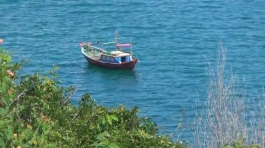 dalgalar üzerinde sallanan küçük ahşap tekne. Bay yeşilliklerle çevrilidir. Mavi deniz hafif bir dalga vardır.