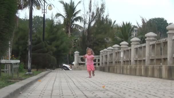 Κορίτσι που τρέχει κατά μήκος μιας διαδρομής σε ένα πάρκο. Κορίτσι στο φόρεμα περπατώντας στον παραλιακό δρόμο — Αρχείο Βίντεο