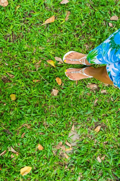 Pie femenino en sandalias sobre una hierba verde — Foto de Stock
