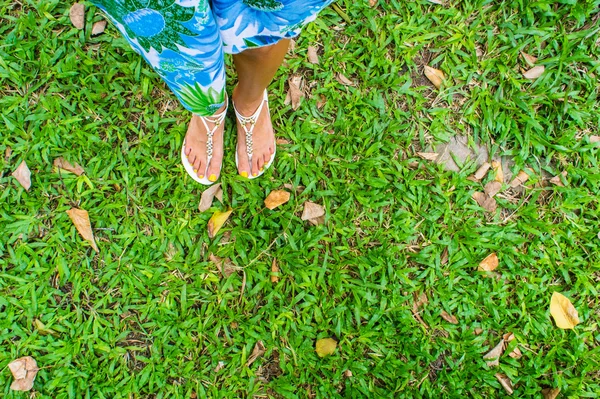 Pie femenino en sandalias sobre una hierba verde — Foto de Stock