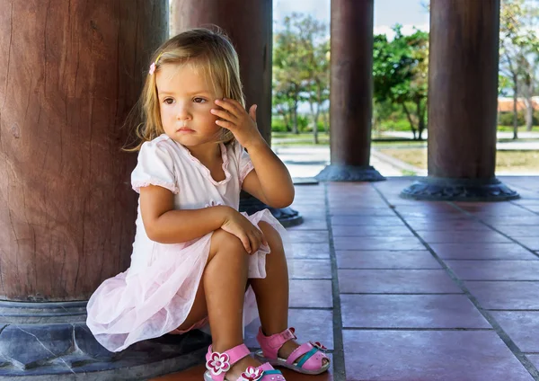 Malá dívka sedí u sloupce — Stock fotografie