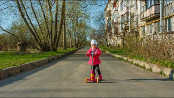 Симпатичная маленькая девочка на скутере в городе, детский спорт. осень, в пальто — стоковое видео