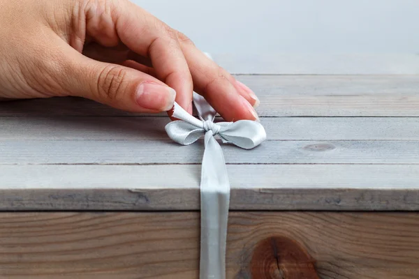 Vrouwelijke hand unties het lint op houten geschenkdoos — Stockfoto