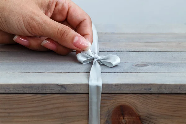 Vrouwelijke hand unties het lint op houten geschenkdoos — Stockfoto