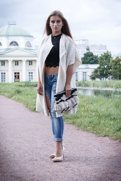Мода на красивую молодую хипстершу, позирующую на фоне и дворца в джинсовой обуви, длинном кардигане . — стоковое фото