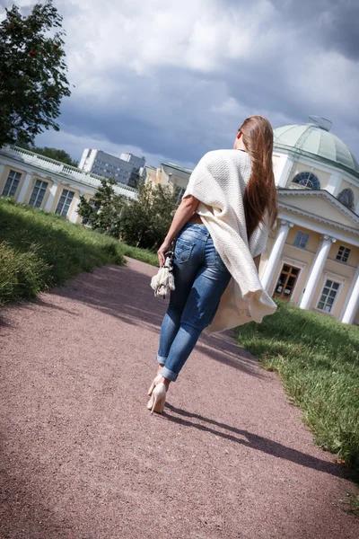 Donna posa sullo sfondo e palazzo in jeans scarpe, lungo cardigan. è tornata . — Foto Stock