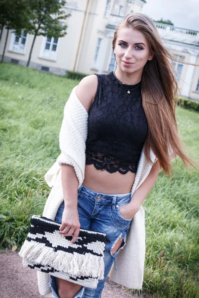 Moda di bella bella giovane donna hipster in posa sullo sfondo e palazzo in scarpe jeans, lungo cardigan . — Foto Stock