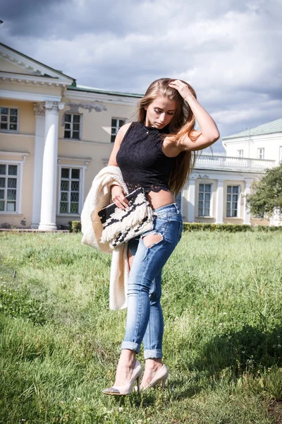 Moda di bella bella giovane donna hipster in posa sullo sfondo e palazzo in scarpe jeans, lungo cardigan . — Foto Stock