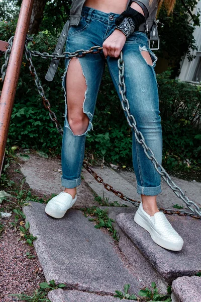Kadın bacakları yırtık kot pantolon, yakın çekim, paslı bir zincir tutan kız. — Stok fotoğraf