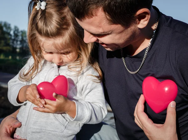 man and baby holding a two red plastic heart. father hugs the daughter