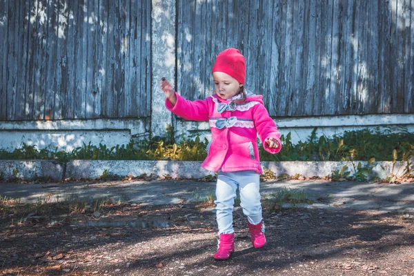 Malá holčička v růžový kabát, džínách a botách chodit do parku — Stock fotografie