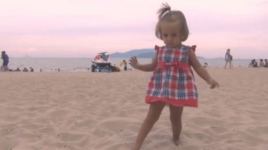 kırmızı mavi elbiseli güzel bebek kameranın içine kum ayak atar. kum uçan uzak kamera