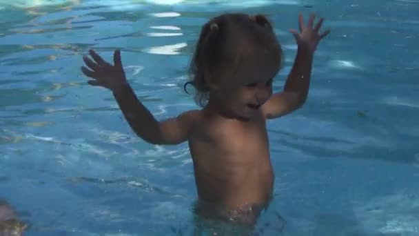 Beautiful baby is happy, laughs and claps her hands standing by the pool with blue clear water. Slow motion — Stock Video