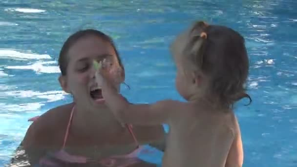 Young beautiful girl puts leaf on the nose, and the baby takes it. they sit in the pool and laughing — Stock Video