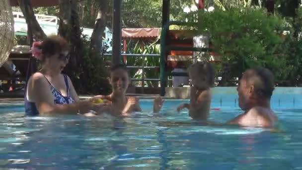 Les Européens heureux famille jouer avec un bébé dans une piscine. jeune fille et la femme jetant le bébé petite boule jaune dans la piscine. homme flottant à proximité et aime les regarder — Video