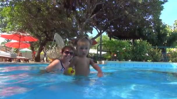 Em uma piscina bebê joga uma bola amarela na câmera, água azul voando para a câmera. Movimento lento — Vídeo de Stock