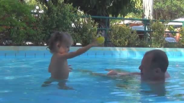 Dans une piscine un beau bébé lançant une boule jaune à grand-père. pulvérisation d'eau volant sur le visage d'un homme, il a vissé ses yeux . — Video