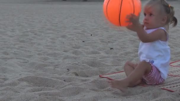 Na plaży piękne dziecko w biały T-shirt rzuca duży pomarańczowy piłkę w kierunku" — Wideo stockowe