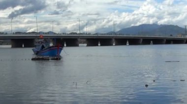 Vietnamca tekne çapa Nehri üzerinde mavi. Balıkçılar balık ağlarına tekne içine atma. arka planda Oto ve motosiklet hareketli bir köprü var