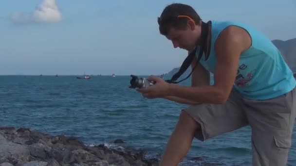 Young man taking pictures on the camera on a rocky seashore — Stock Video