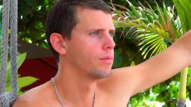 Молодой человек сидит на веревке качается в джунглях и думает о жизни — стоковое видео
