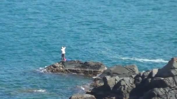 Ein einzelner Mann fischt mit einem riesigen Stein im offenen Meer. Das Meer ist sauber und blau. — Stockvideo