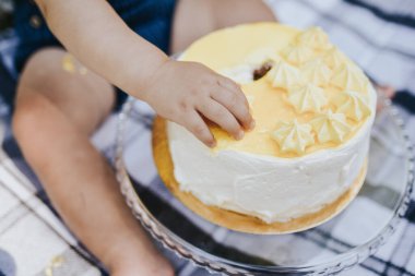 Çocuğun eli pastanın üstünde. Çocuk pastayı yemek istiyor.
