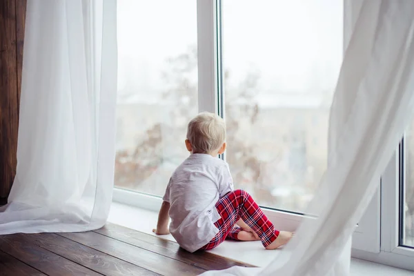 Pencereden dışarı bakan pijamalı çocuk.
