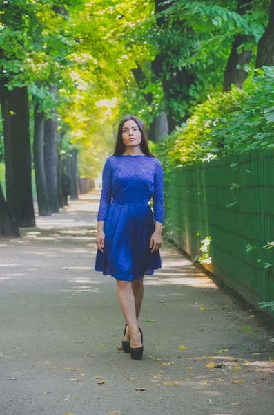 Menina bonita em vestido azul andando no parque entre grandes árvores — Fotografia de Stock