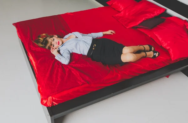 The girl with the blue eyes tempting lies on the bed in a shirt with a wide neckline — Stock Photo, Image