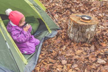 Bir sonbahar günü bir çocuk bir kamp alanında çadırda kahvaltı yapıyor.