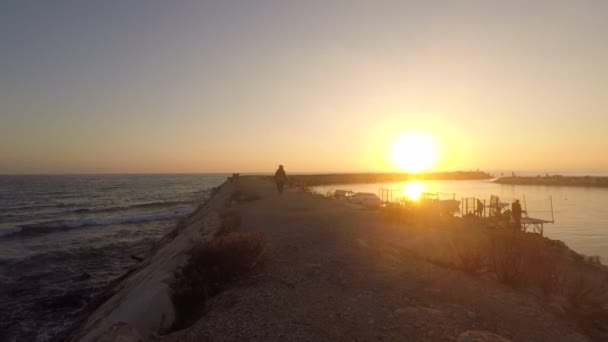 Au coucher du soleil un pêcheur marche le long de la jetée — Video