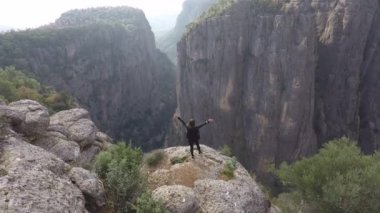 Kanyonun yukarısında elleri havada bir insan gezgin duruyor.