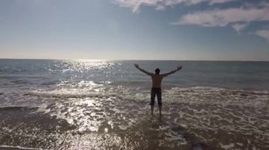 Kumsalda genç bir adam suya girdi ve güneşlenerek ellerini kaldırdı ve mutluydu.