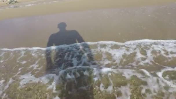 Het zand gewassen door de golven een man schaduw steekt zijn handen op — Stockvideo