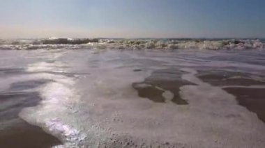 Kumlu bir sahilde, dalgalar yukarıdan geliyor.