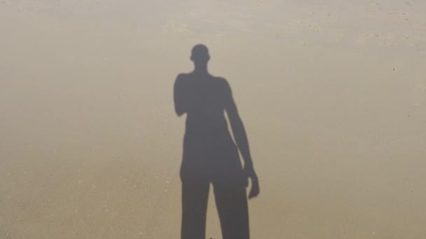 De op het zand, de schaduw van een man met zijn hand omhoog in de lucht — Stockvideo
