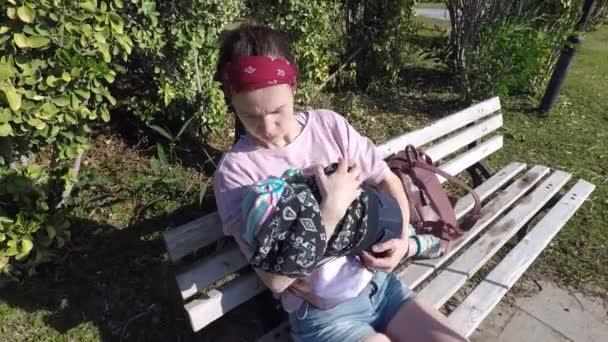 A kislány a kisbabával egy padon ül egy nyári napon. — Stock videók