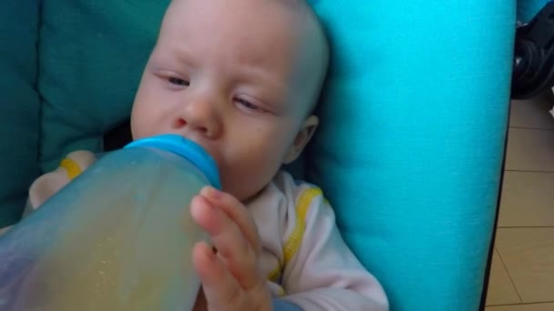 O bebê deitado em um carrinho come comida de bebê de uma garrafa — Vídeo de Stock