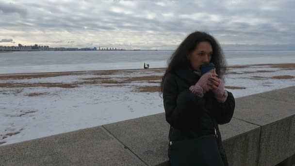 El invierno en el terraplén, una chica triste con un vaso de café — Vídeos de Stock