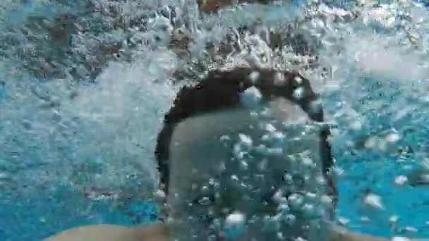 muž v bazénu plave pod vodou