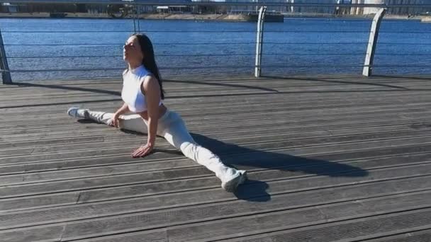 Flickan en solig morgon är engagerad i fitness stretching på vallen — Stockvideo