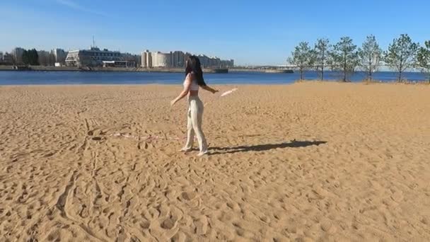 В сонячний ранок дівчина на піщаному пляжі робить вправи з гімнастичною стрічкою — стокове відео