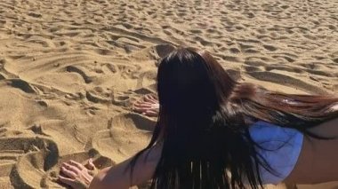 Kumlu bir sahilde bir kız yoga esneme egzersizleri yapıyor.