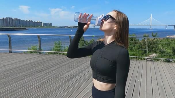 La deportista bebe agua durante una sesión de entrenamiento en el terraplén — Vídeos de Stock