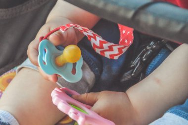 Emzik ve oyuncak tutan bir bebek elinin yakın çekimi.