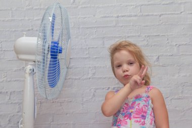 Elektrikli vantilatörün önündeki kız sıcak bir yaz gününde serin rüzgarın tadını çıkarıyor.