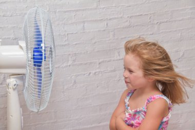 Elektrikli vantilatörün önündeki kız sıcak bir yaz gününde serin rüzgarın tadını çıkarıyor.